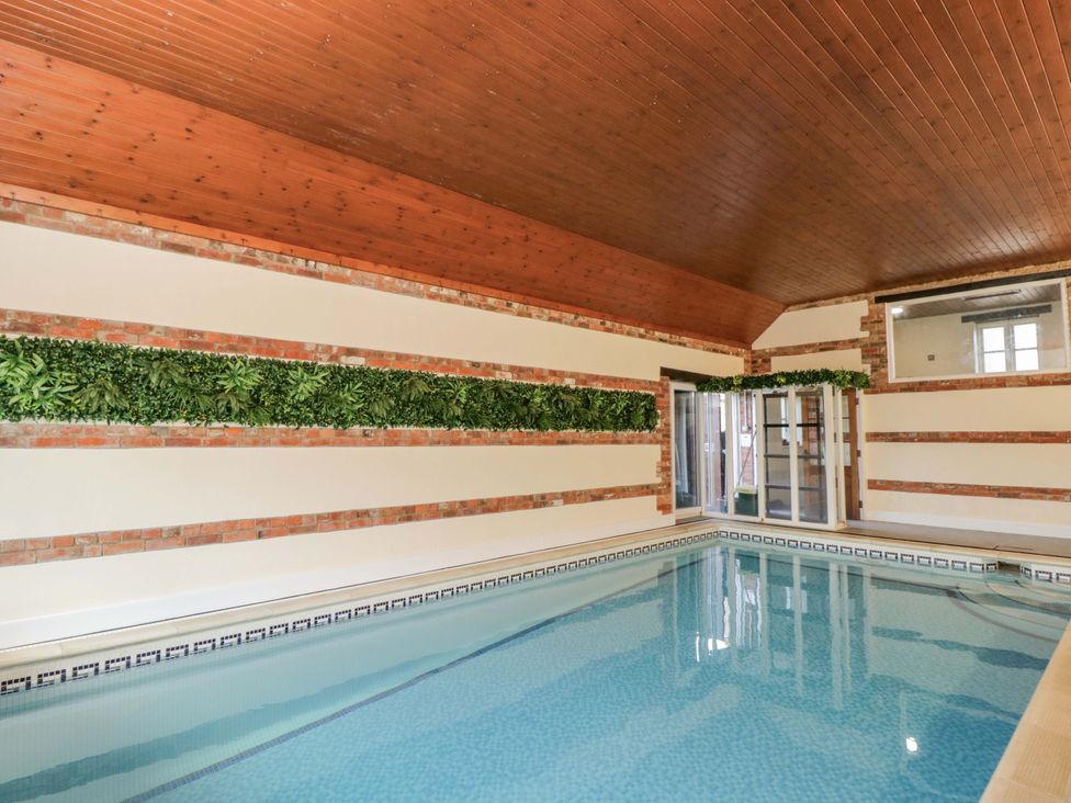 An indoor swimming pool with plants and windows at Barn Cottage in Frome