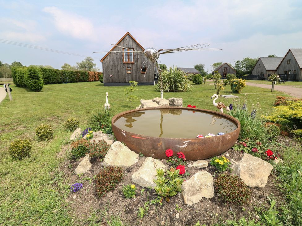 A pond surrounded by flowers and rocks with a house in the background at James Ville Marina Lodge 22, Brigg