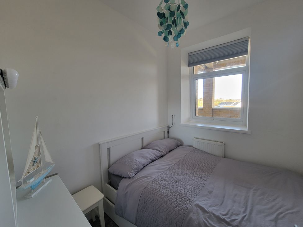 A bedroom with a bed, window, and lamp at Plas Darien no 28 in Trearddur Bay