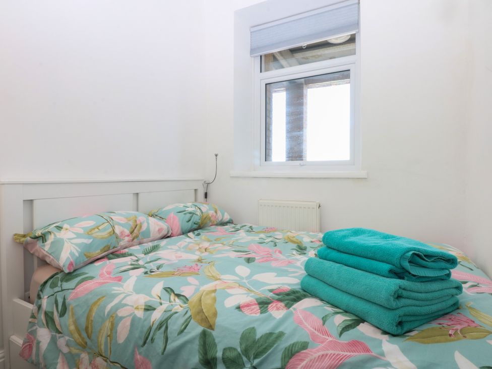 A bedroom with a bed, pillows, towels, and a window at Cwtch y Môr Trearddur Bay