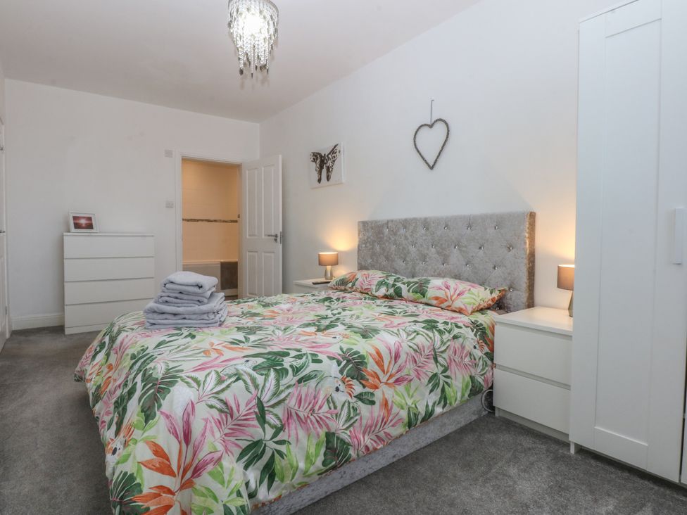 A bedroom with a bed, nightstand, dresser and decor at Cwtch y Môr in Trearddur Bay