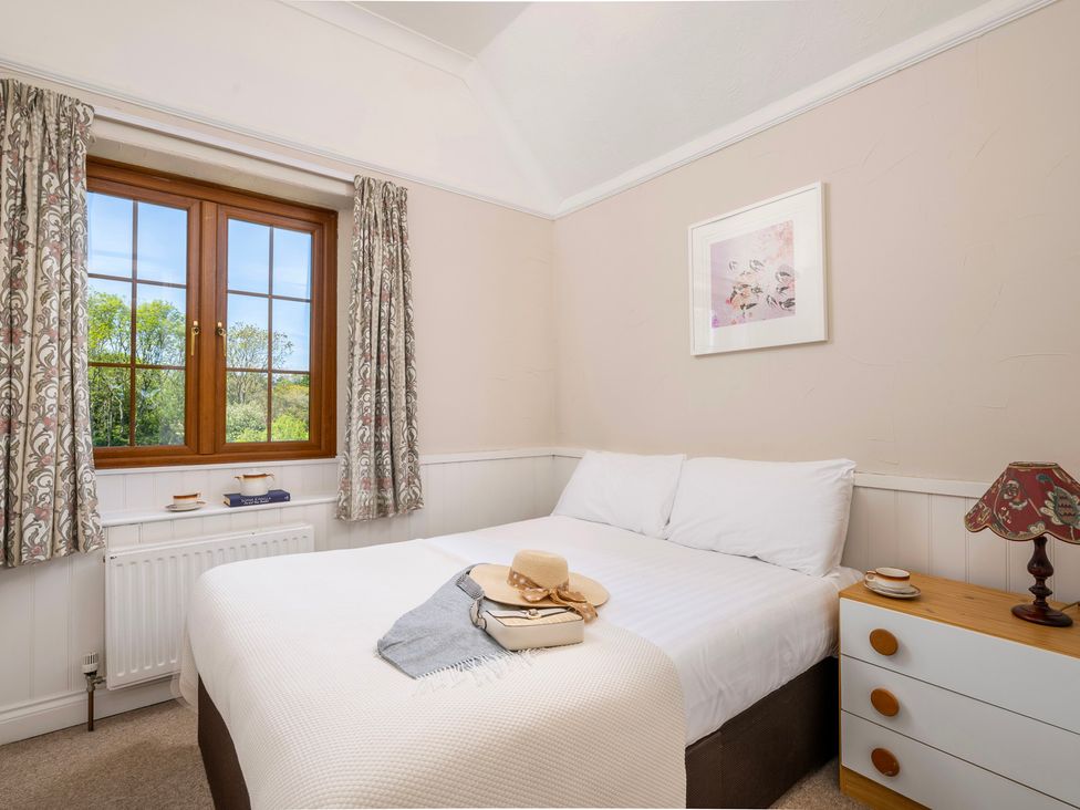 A bedroom with a bed, window, nightstand, and lamp at The Hayloft Budock Water near Falmouth