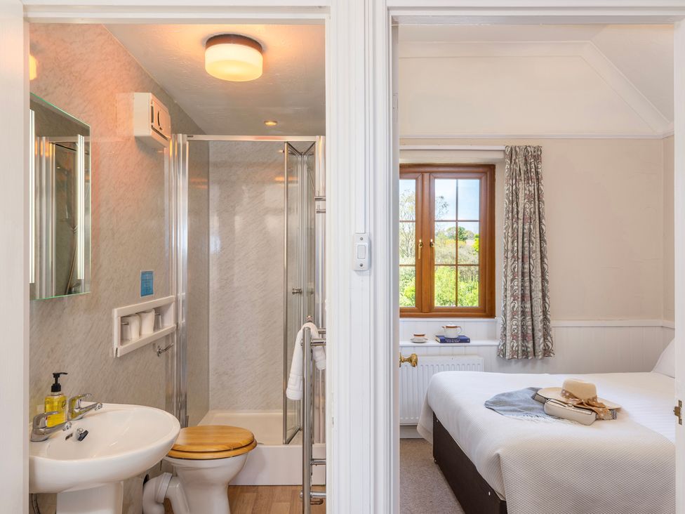 A bathroom with shower and sink beside a bedroom with window and bed at The Hayloft Budock Water near Falmouth