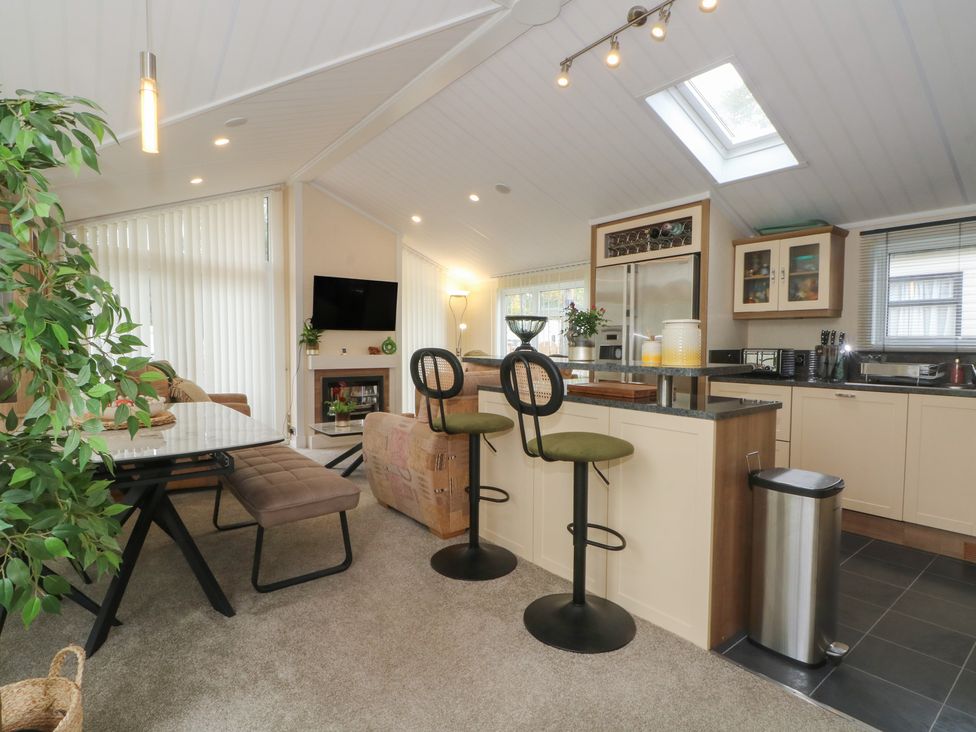 A living room with kitchen features including bar stools and a dining table at Labernum in Lytham St. Annes