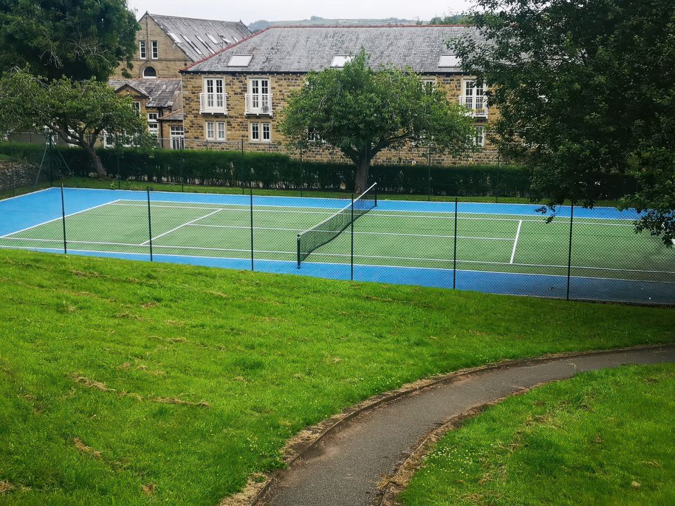 A tennis court with a fence and building in the background at Steam View Cottage in Haworth