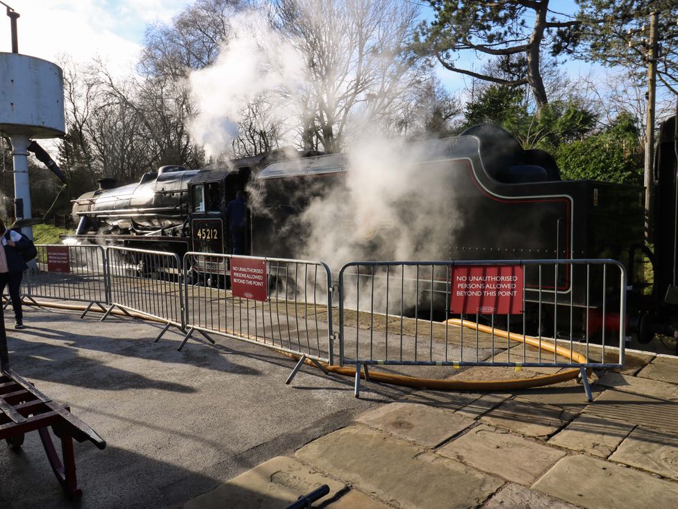 A steam locomotive with smoke, water tower and barriers at Steam View Cottage in Haworth