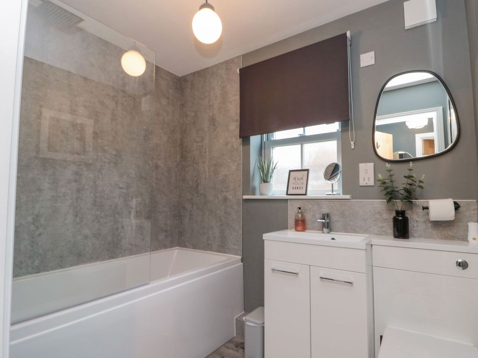 A bathroom with a bathtub, sink, and window at Rosie's Retreat in Filey