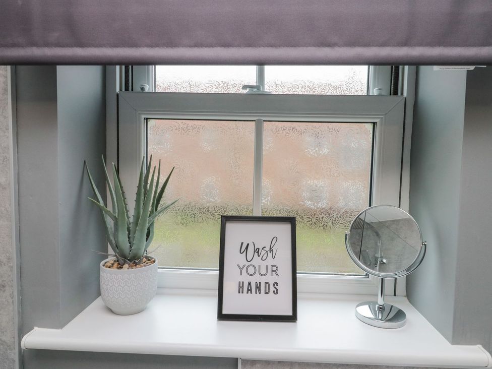 A bathroom window with a plant, sign, and mirror at Rosie's Retreat in Filey