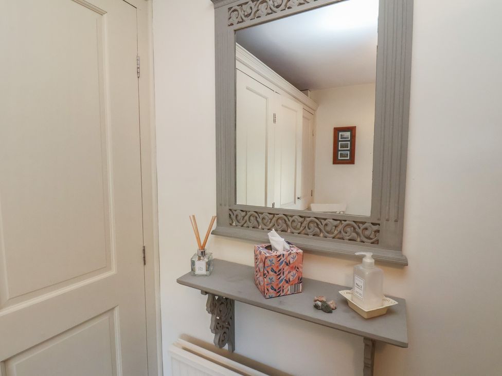 A hallway with a mirror and shelf holding a tissue box and hand wash at Woodbine Cottage in Whitby