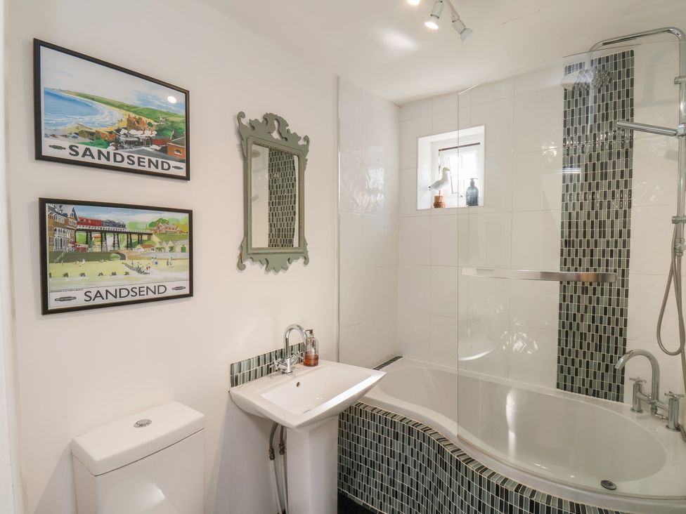A bathroom featuring a bathtub, shower, sink, and decorative wall art at Woodbine Cottage in Whitby