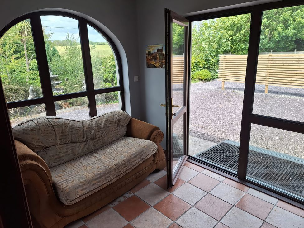 A conservatory with a couch and large windows at Lilly's Bungalow in Timoleague