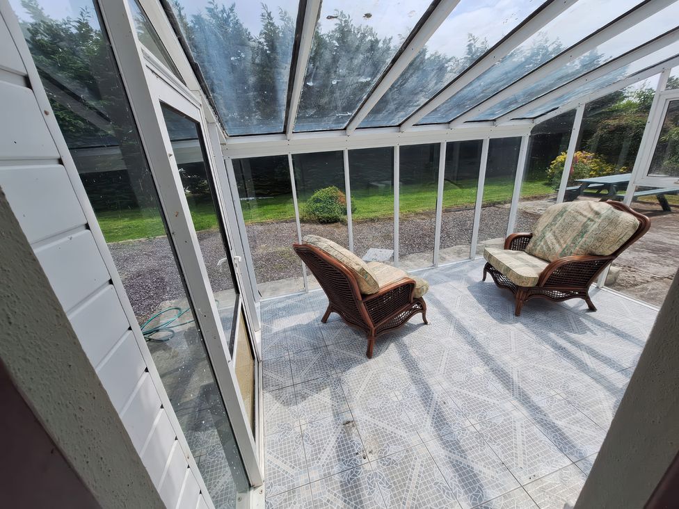 A conservatory with rattan chairs and a garden view at Lilly's Bungalow in Timoleague