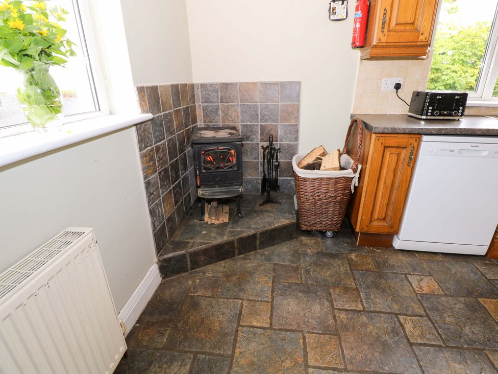 A kitchen with a wood stove, logs, and a dishwasher at CARROWREAGH