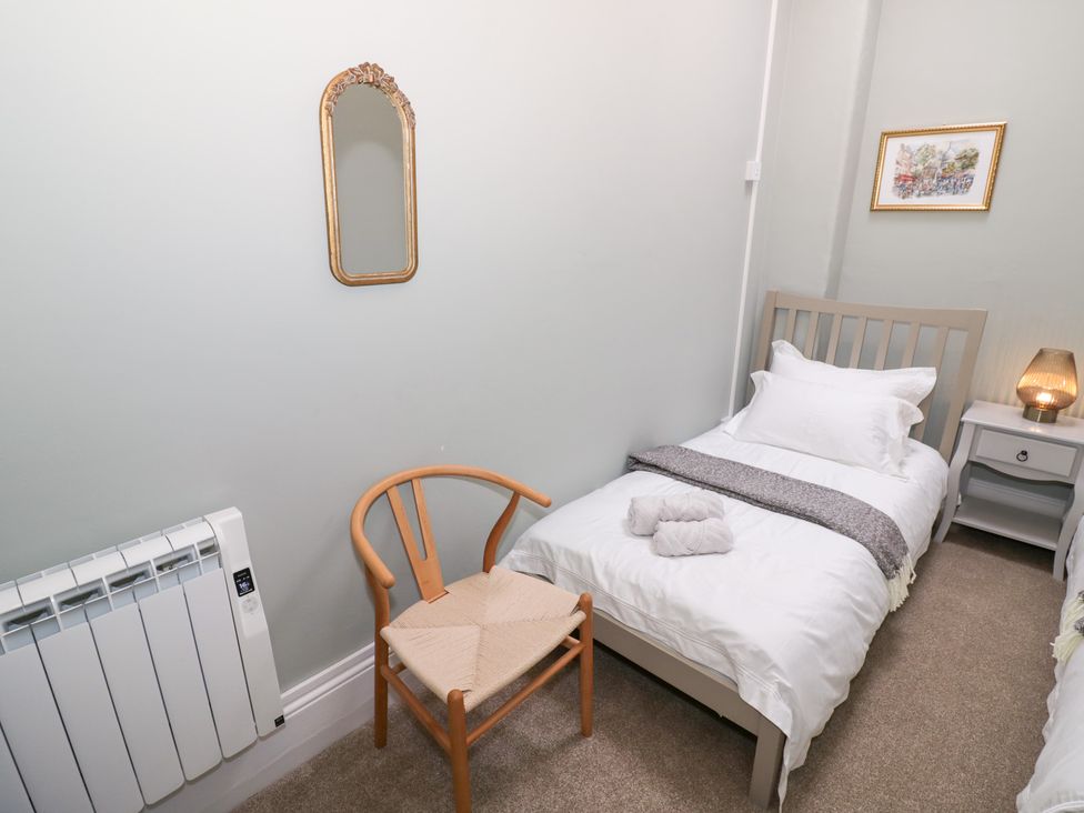 A bedroom with a bed, chair, nightstand and mirror at 12 Montpellier Arcade in Cheltenham