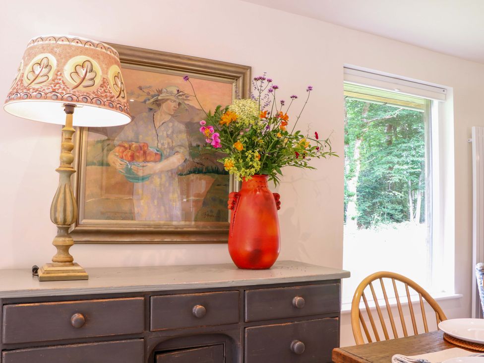 A dining room with a lamp and vase of flowers at Lakeside Lodge Witherenden Hill near Burwash