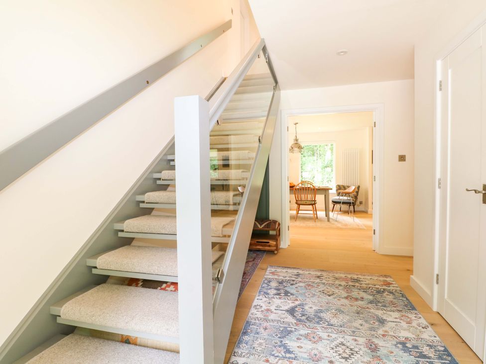 A hallway with a staircase and a dining area in the background at Lakeside Lodge witherenden Hill near Burwash