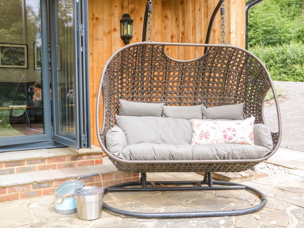 A hanging chair with cushions by a wooden wall at Lakeside Lodge in Witherenden Hill near Burwash