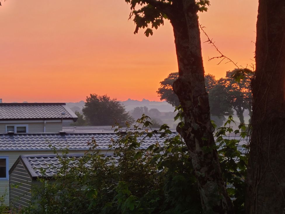 A view of rooftops and trees under a colorful sky at The Maples, no. 56 St. Austell