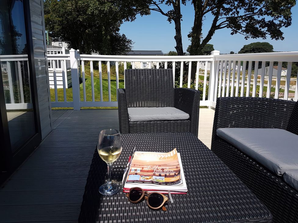 A deck with seating, a wine glass, a book, and sunglasses at The Maples, no. 56 St. Austell