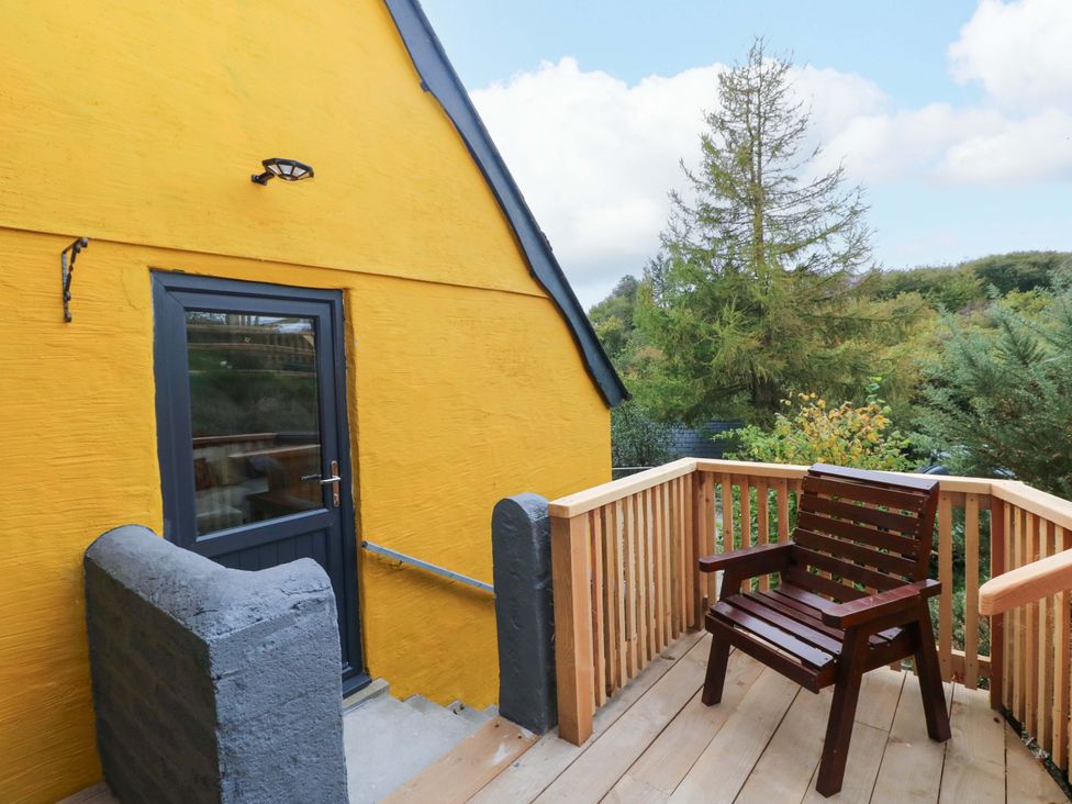 An outdoor deck with a wooden chair and a yellow wall at Pendre Barn Star near Cenarth