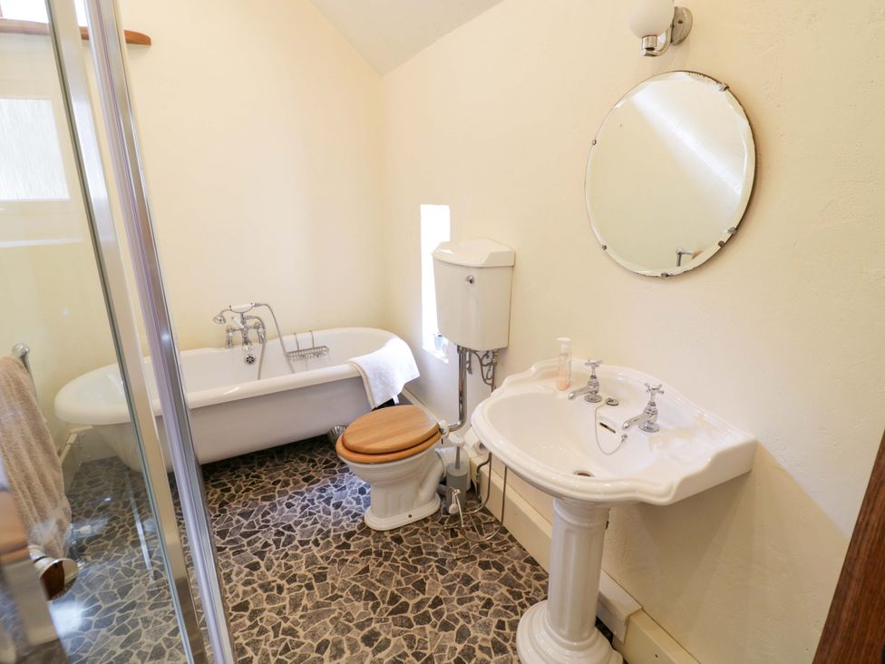 A bathroom with a bathtub, sink, toilet, and mirror at Fern Cottage