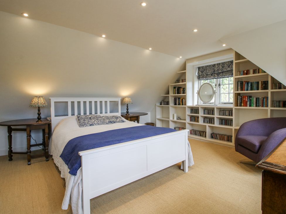 A bedroom with a bed, bookshelf, and chair at Garden Cottage in Wellington Heath near Ledbury