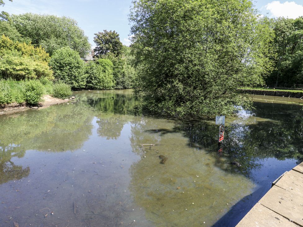 A pond surrounded by trees and a caution sign at Little Birchinlea Glossop