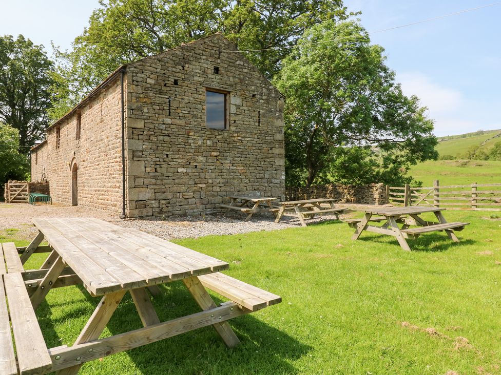 An outdoor area with picnic tables in front of a stone building at East Barn Bunkhouse