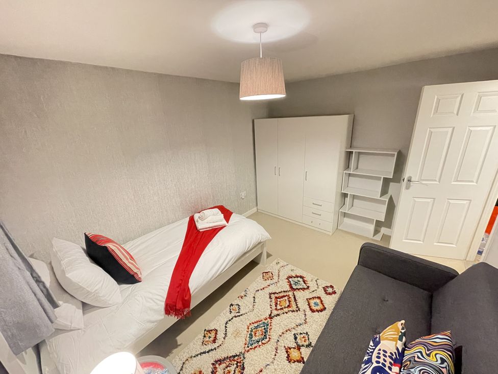 A bedroom with a bed, wardrobe, shelf unit, and sofa at Derby Den in Breadsall near Derby