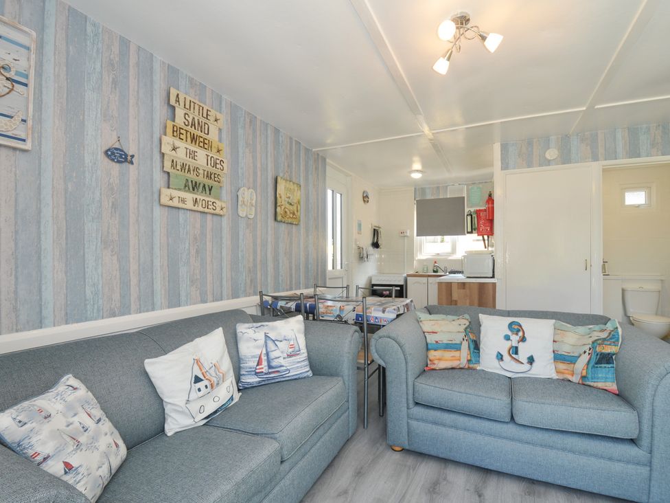 A living room with a sofa and kitchen area at 13 Hillside Bude