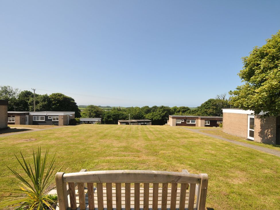 An outdoor area with a bench, grass, and surrounding buildings at 13 Hillside in Bude