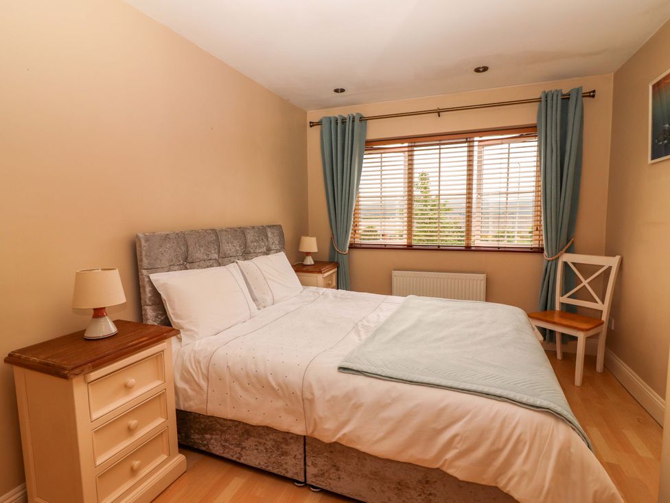 A bedroom with a bed, nightstand, lamp, window, and a chair at 51 Woodview Park in Tralee, County Kerry
