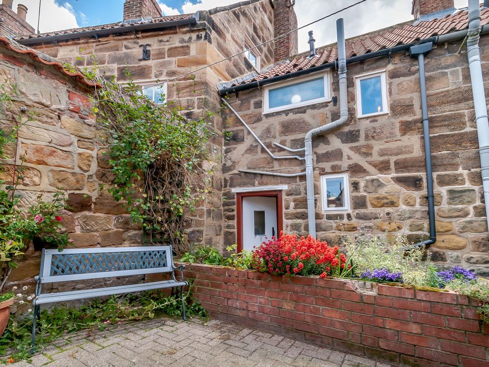 A garden with a bench, flower bed and brick wall at Chimes Cottage in Guisborough