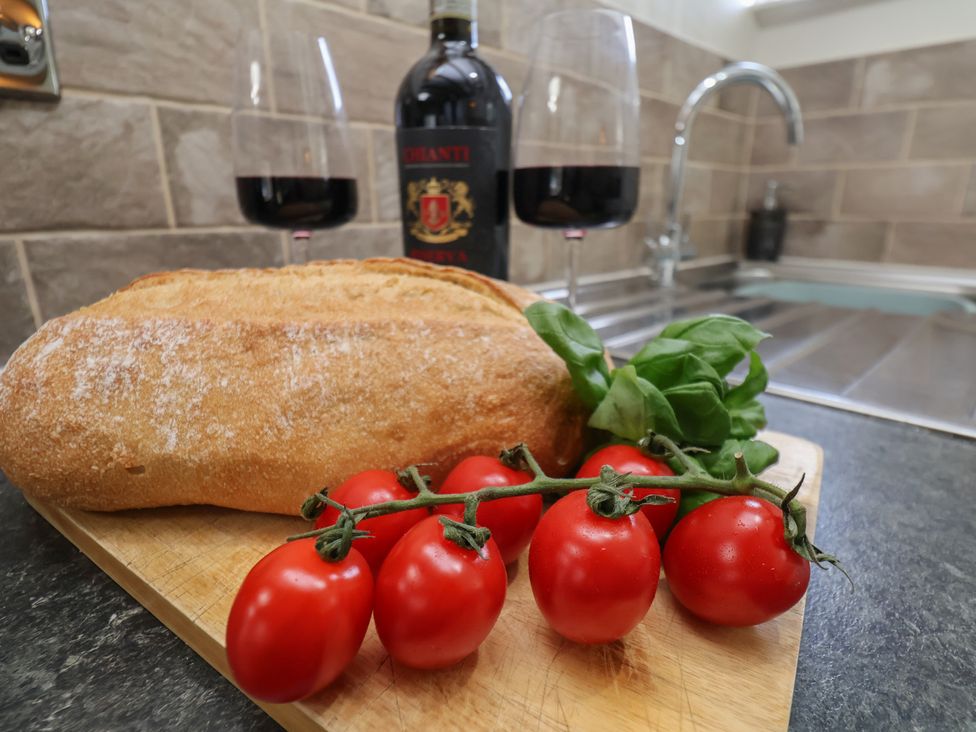 A kitchen with bread, tomatoes, basil, and red wine at Chimes Cottage in Guisborough
