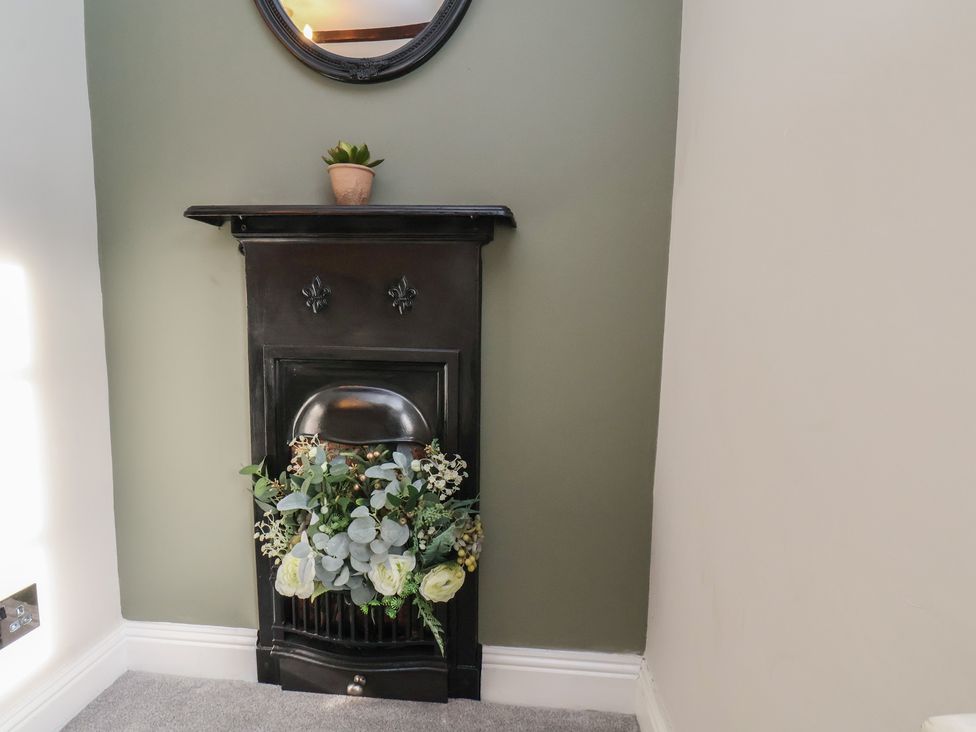 A fireplace with a mirror and flowers at Chimes Cottage in Guisborough