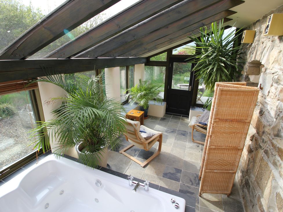 A conservatory with a hot tub and plants at The Dovecote in Fishguard