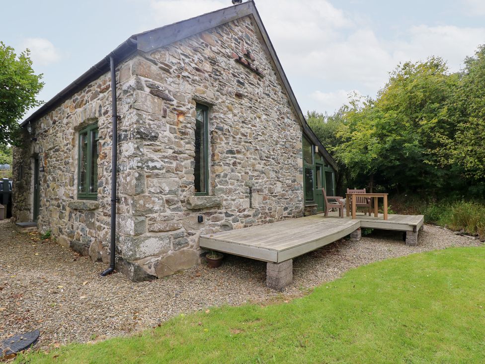 A stone building exterior with a wooden deck and seating at The Dovecote in Llanychaer near Fishguard