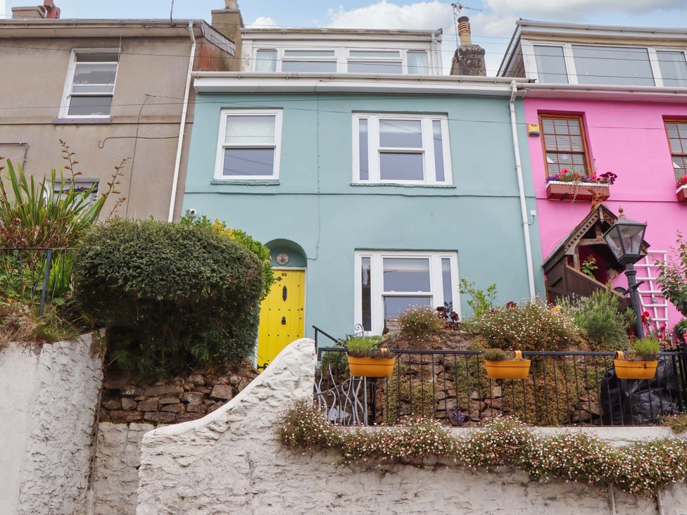 A colorful house with a yellow door and plants in pots at Captains Cottage in Brixham