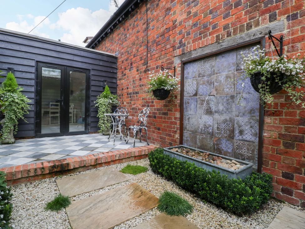 An outdoor area with a table and chairs near a decorative wall fountain at The Sty, Shades Farm near Malmesbury