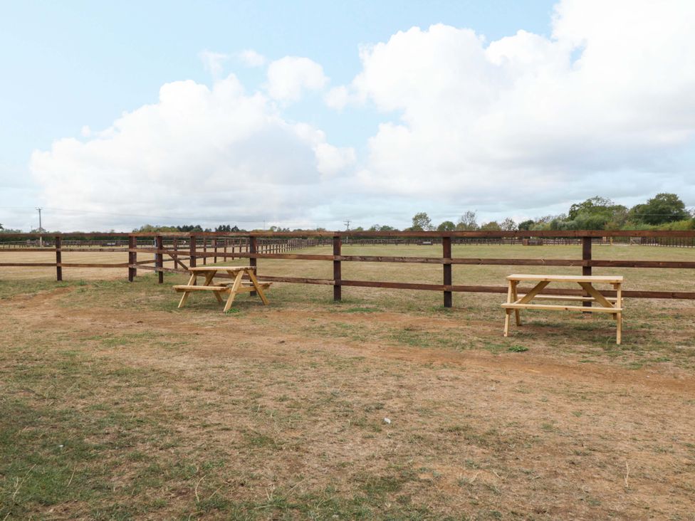 A garden with wooden tables and a fence at Bell 1 Shades Farm near Malmesbury