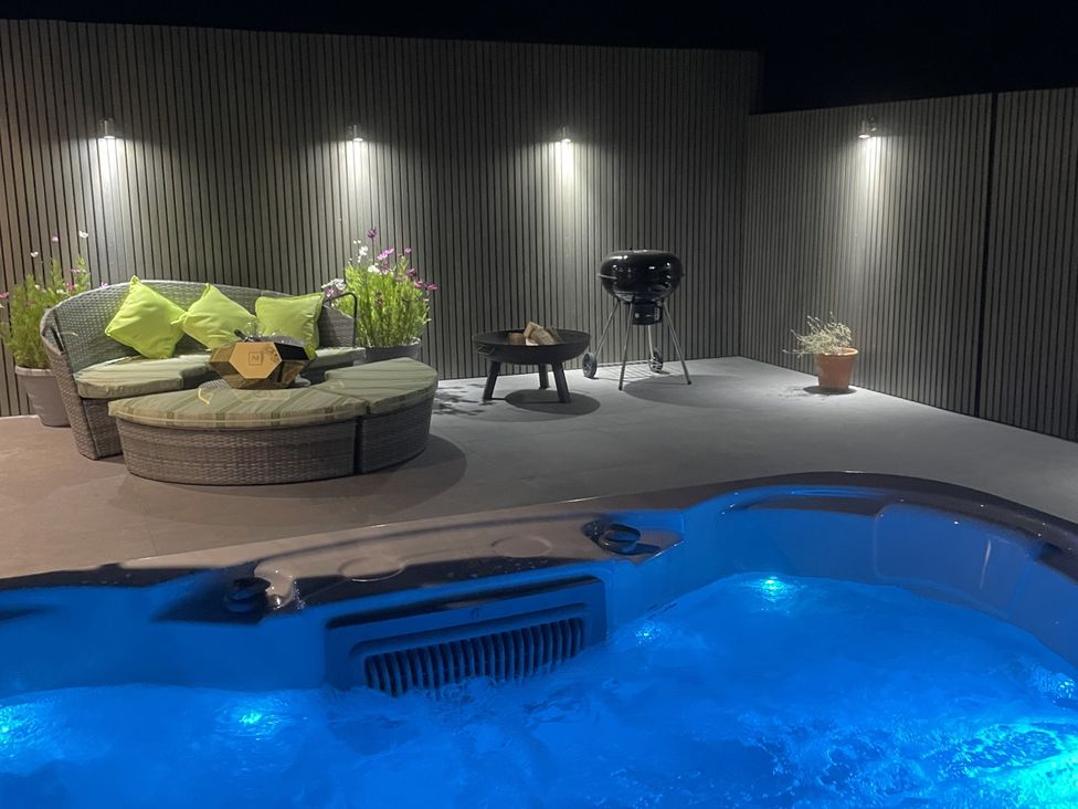 An outdoor area with a hot tub, sofa, grill, and potted plants at Noflash Malpal in Bishop Sutton