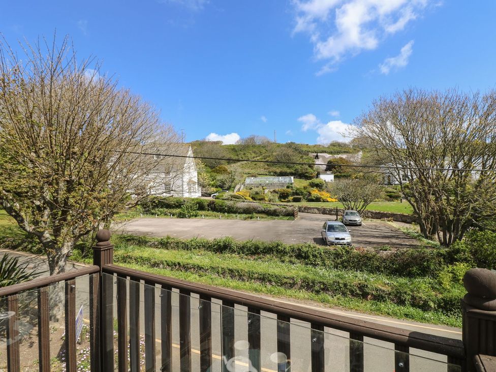 A view of a parking lot and houses from a balcony at Tater-Du in Porthcurno