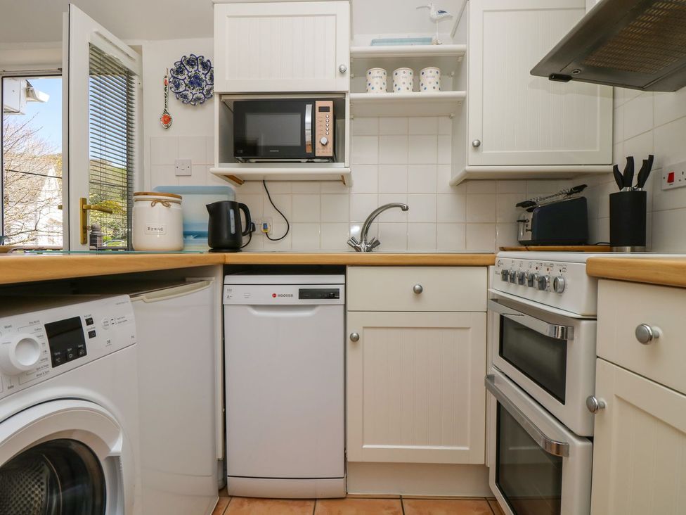 A kitchen with appliances including a washing machine and microwave at Tater-Du in Porthcurno