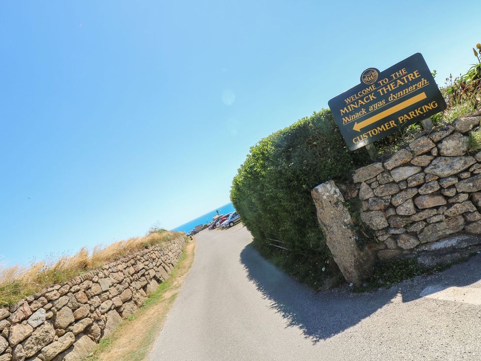 A sign indicating the Minack Theatre with a view of the ocean at Tater-Du in Porthcurno