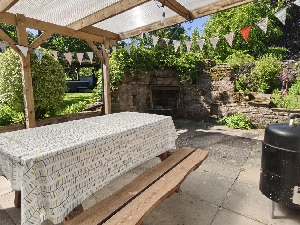 A garden with a table and bench under a wooden canopy at Bush Nook House in Brampton, Cumbria