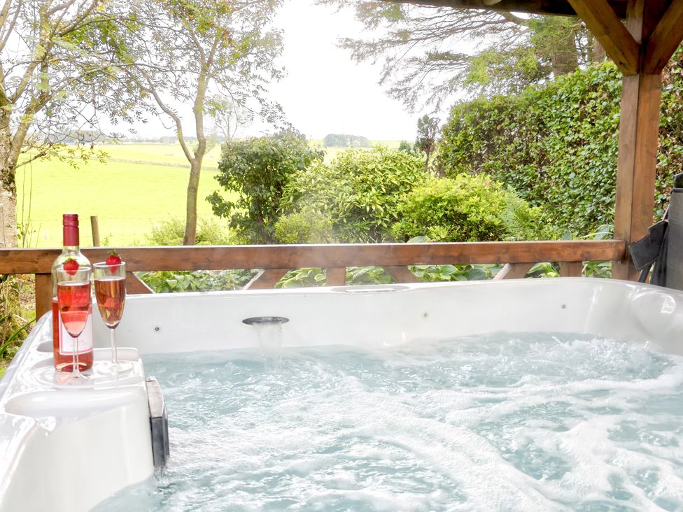 An outdoor hot tub with wine glasses and a bottle at Bush Nook House in Brampton, Cumbria