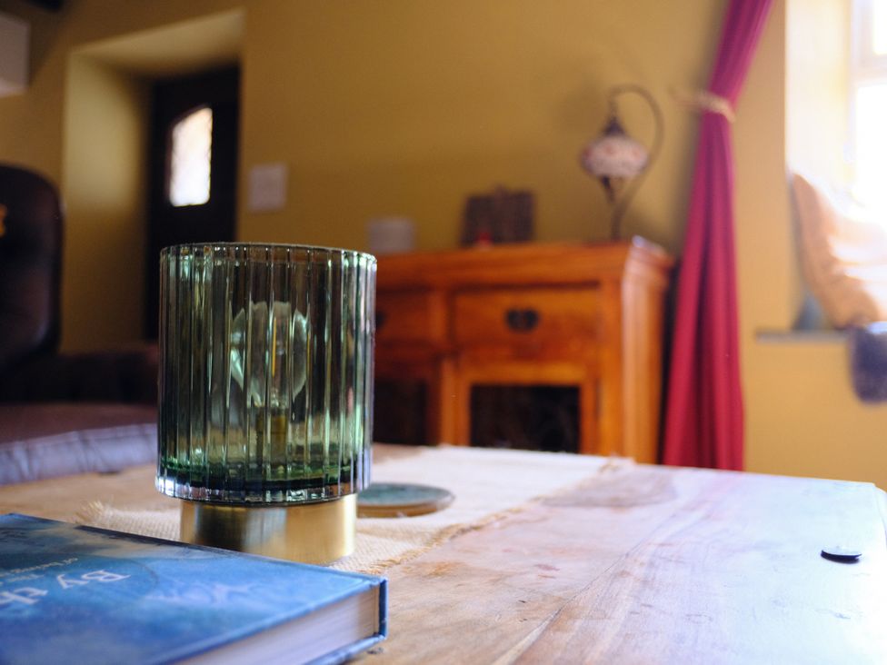 A table with a glass lamp and a book in the living room at Sunnybrae Cottage in Tintagel