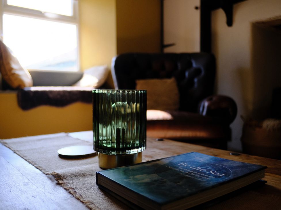 A living room with a candle and a book on a table at Sunnybrae Cottage in Tintagel