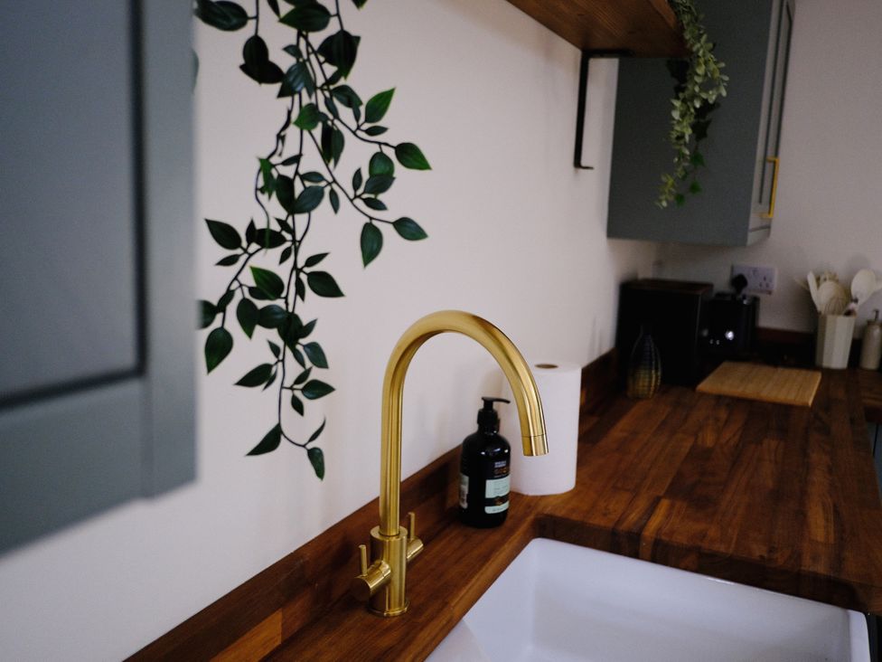 A sink with a gold faucet and soap dispenser in a kitchen at Sunnybrae Cottage in Tintagel