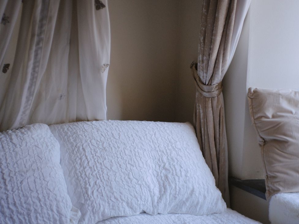 A bed with pillows near curtains at Sunnybrae Cottage in Tintagel